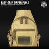 Beige sling bag with American flag patch and easy-grip zipper pulls on a black background.